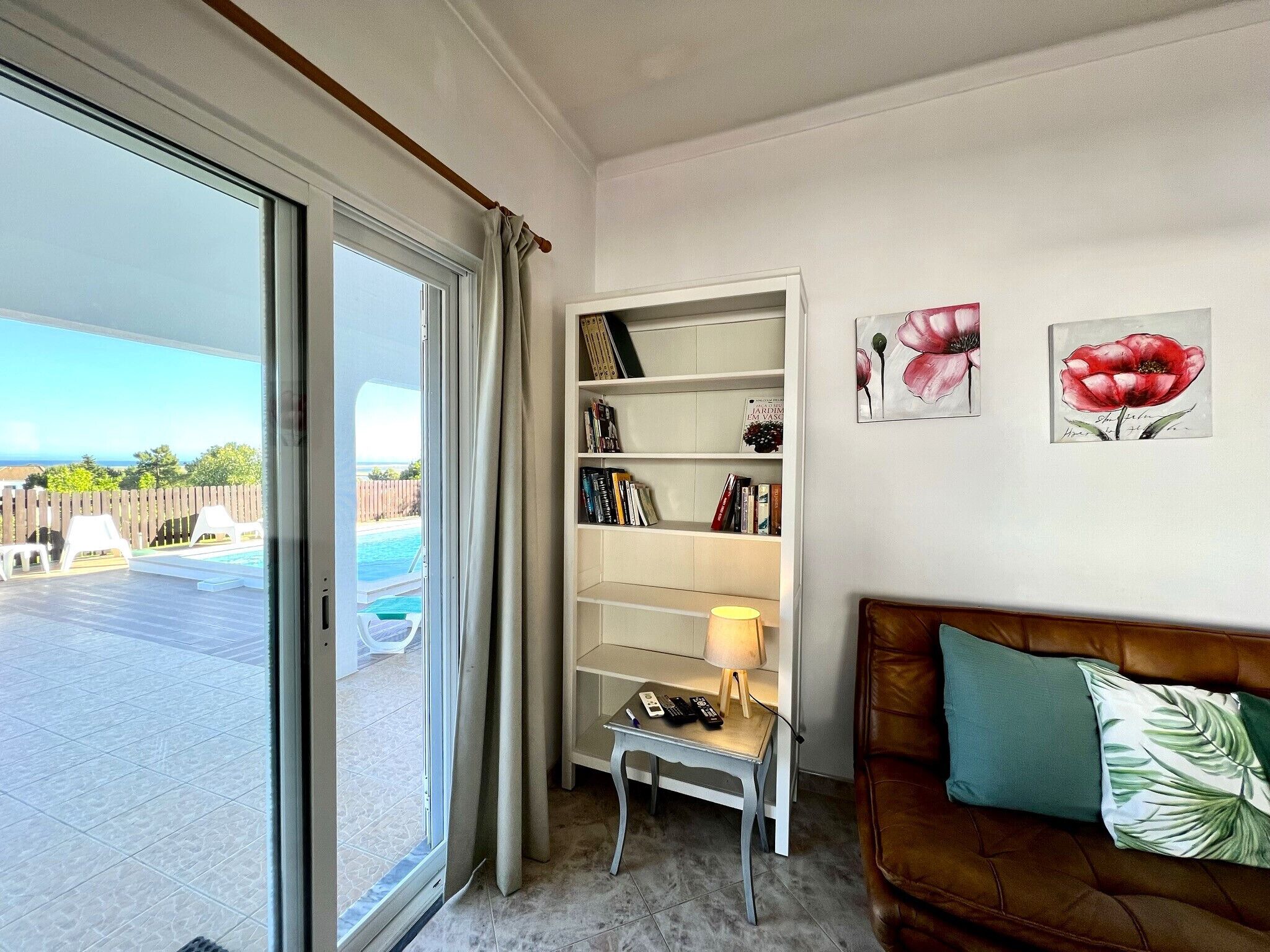 A living room with a large window, a bookshelf, a sofa, and a pool view.