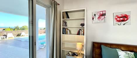 A living room with a large window, a bookshelf, a sofa, and a pool view.