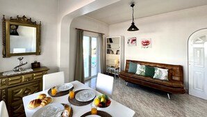 A dining area with a table set for breakfast, a sofa, and a bookshelf. - Tavira Vila Formosa 3 With Pool (Tavira)