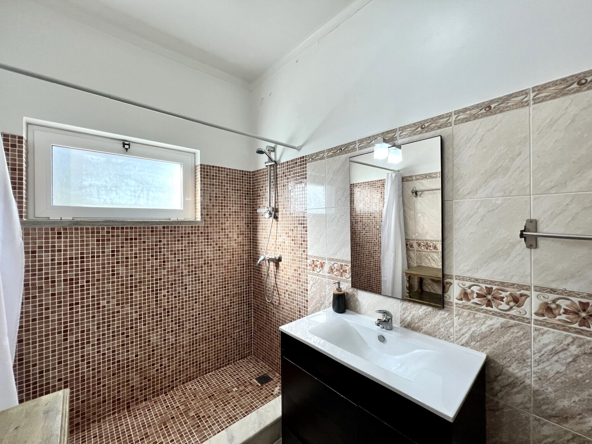 Une salle de bain avec une douche, un lavabo et une fenêtre.