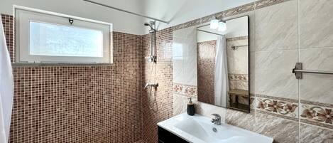 Une salle de bain avec une douche, un lavabo et une fenêtre.
