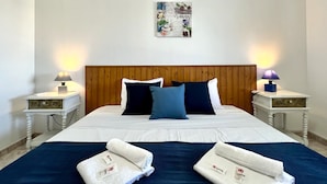 A neatly made bed with a wooden headboard, two bedside tables with lamps, and a wall art piece above the bed. - Tavira Vila Formosa 3 With Pool (Tavira)