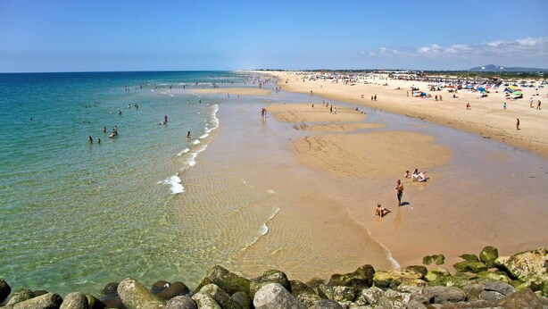 A beach with clear water, sandy shore, and rocks in the foreground. - Tavira Vila Formosa 3 With Pool (Tavira)