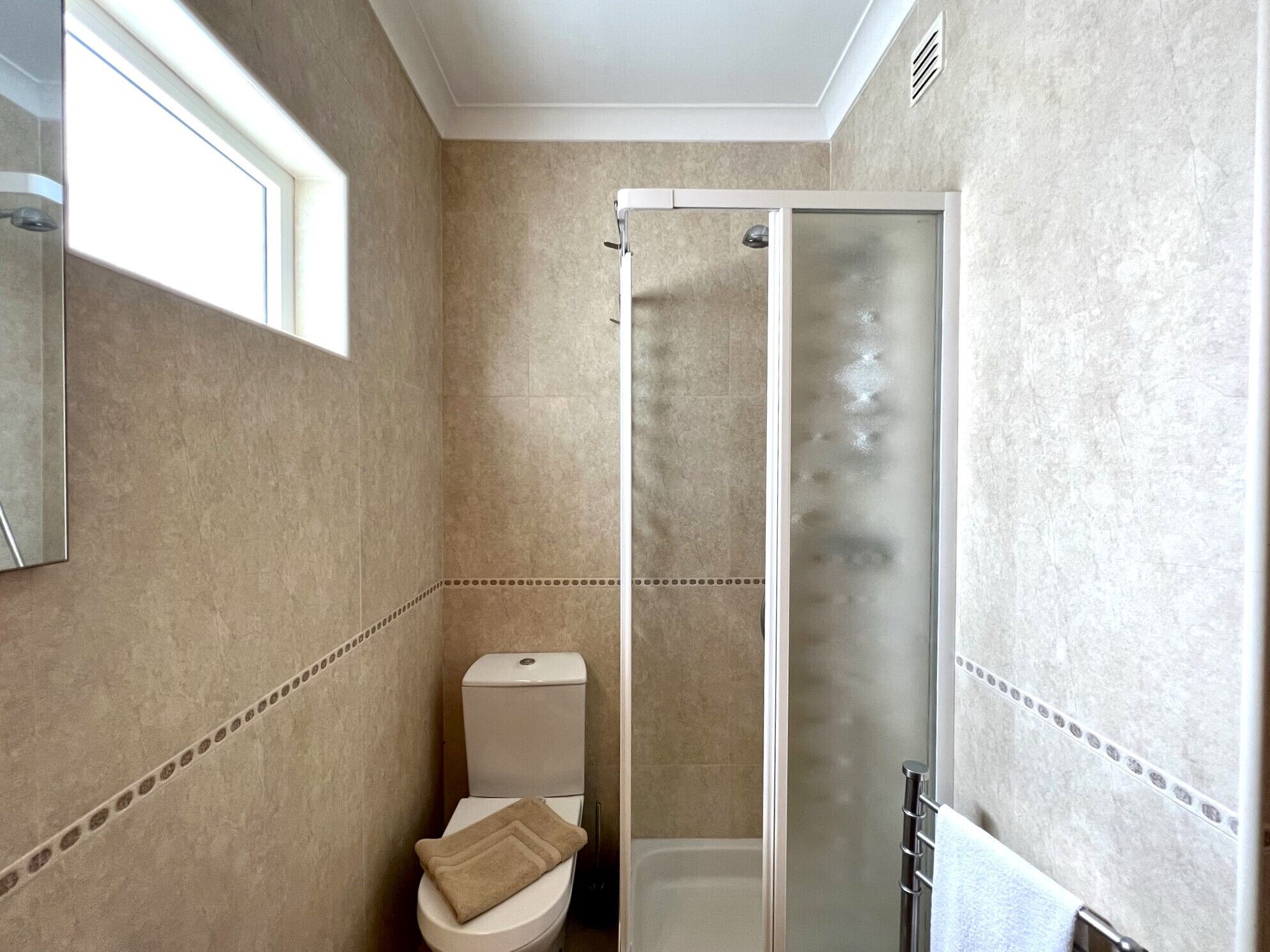 A bathroom with a toilet, a shower with a glass door, and a towel rack.