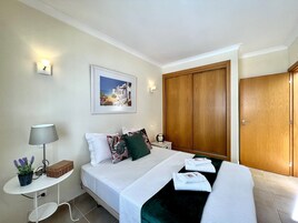 Un dormitorio ordenado con cama, almohadas, una mesita de noche con lámpara, un cuadro en la pared y un armario.