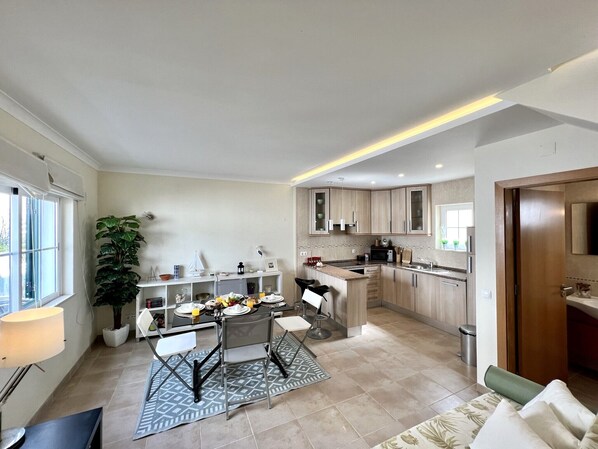 A modern kitchen with a dining area, featuring a central island, built-in cabinets, and a large window providing natural light.