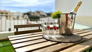 Ein Metallkübel mit einer Champagnerflasche, zwei Gläsern mit Erdbeeren und einer gewebten Unterlage auf einem Holztisch im Freien.
