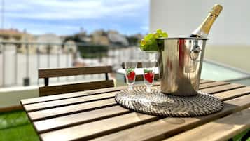 Ein Metallkübel mit einer Champagnerflasche, zwei Gläsern mit Erdbeeren und einer gewebten Unterlage auf einem Holztisch im Freien.