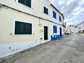 Una calle estrecha con edificios de fachadas azules y blancas, una puerta a la vista y un coche estacionado.