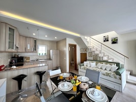 A modern kitchen with a dining area, a staircase, and a living room with a sofa.