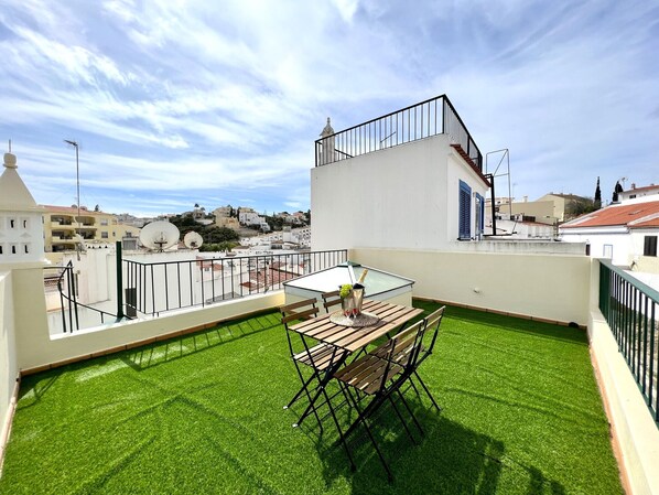 A rooftop terrace with a table and chairs, a small garden area, and a view of the cityscape.