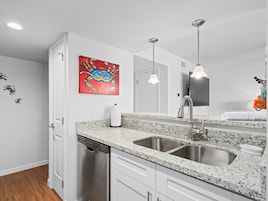 Una cocina moderna con armarios blancos, encimeras de granito, un lavamanos de acero inoxidable y un cuadro colorido en la pared.
