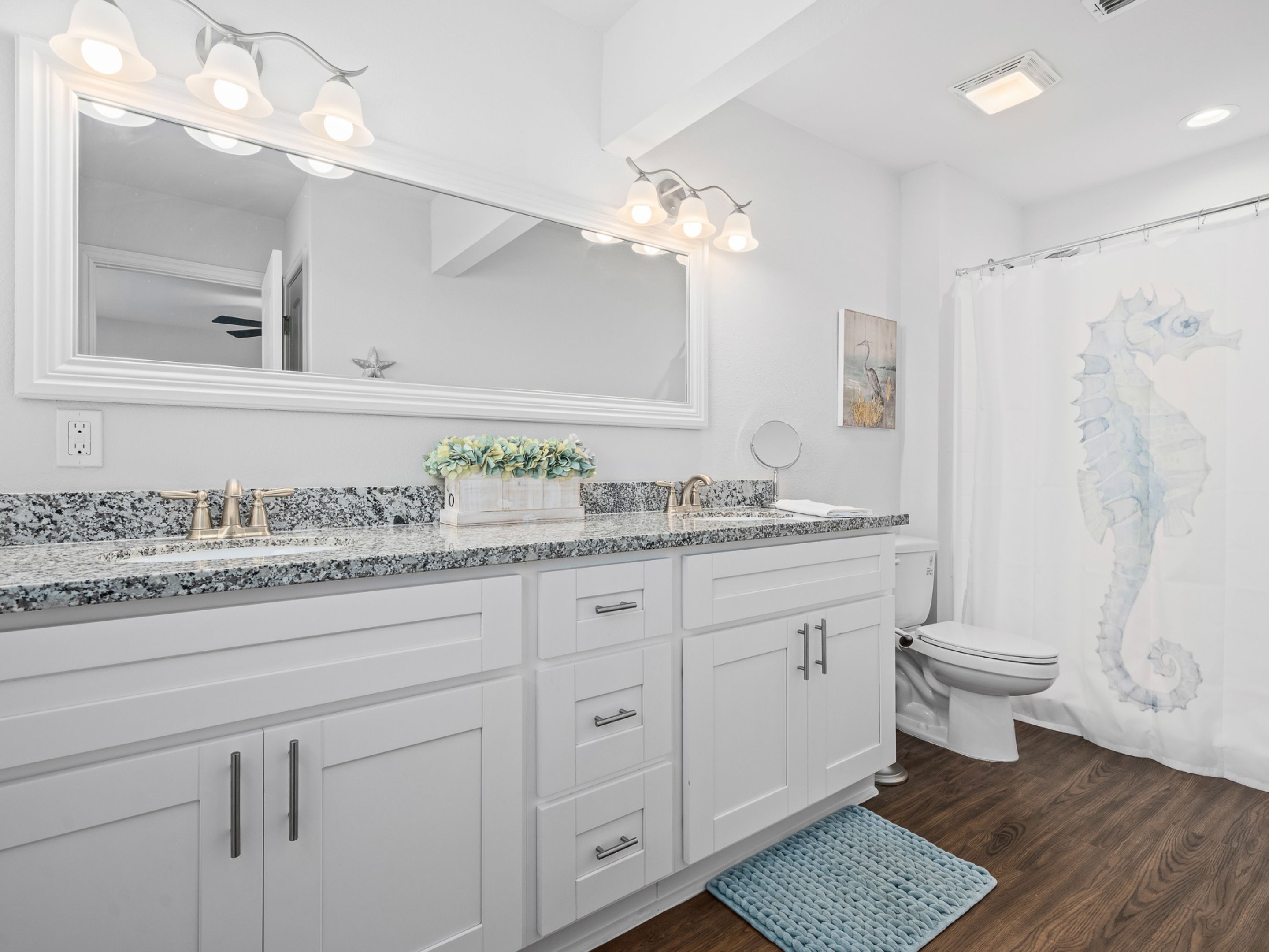 A bathroom with a white vanity, a large mirror, a sink with a granite countertop, a toilet, and a shower curtain with a seahorse design.