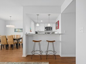 A modern kitchen with white cabinets, a microwave, and a dining area with wicker chairs and a table.