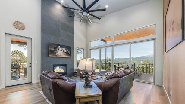 A spacious living room with a fireplace, leather sofas, a wooden coffee table, and a large window offering a scenic view. - Viewtopia by Ruidoso Vacation Rentals (Ruidoso)