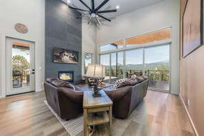 A spacious living room with a fireplace, leather sofas, a wooden coffee table, and a large window offering a scenic view. - Viewtopia by Ruidoso Vacation Rentals (Ruidoso)