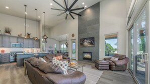 A spacious living area with a large brown leather sofa, a fireplace, and a view through large windows. - Viewtopia by Ruidoso Vacation Rentals (Ruidoso)