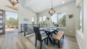A dining area with a wooden table, chairs, and benches, a staircase, and large windows with a view of trees. - Viewtopia by Ruidoso Vacation Rentals (Ruidoso)