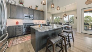 A modern kitchen with dark cabinets, a central island with stools, and pendant lighting. - Viewtopia by Ruidoso Vacation Rentals (Ruidoso)