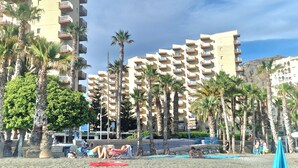 A beachfront hotel with multiple floors, palm trees, and a swimming pool.