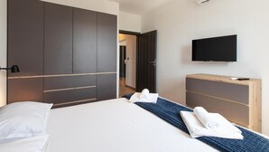 Hotellihuone, jossa on sänky, seinälle asennettu televisio ja vaatekaappi.