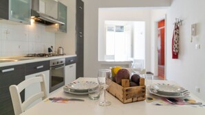 Una cocina moderna con armarios blancos, una mesa de comedor dispuesta con platos, vasos y una cesta de fruta.