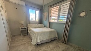 Ein Schlafzimmer mit einem Bett, einem Nachttisch, einem Fenster mit Vorhängen und einem Wandspiegel.