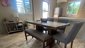 Ein Essbereich mit einem Holztisch und Bänken, eine Küche im Hintergrund und ein Fliesenboden.