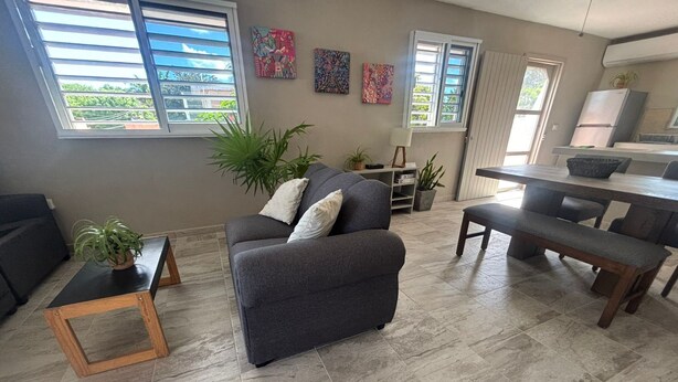 Ein Wohnzimmer mit Sofa, Couchtisch, einem Esstisch mit Bänken und einer Küchenzeile mit Kühlschrank.