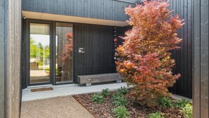 A modern building with a dark wooden facade, a glass entrance, and a bench outside. - 3 bedroom cozy home in Børkop (Børkop)