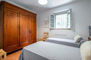 Ein Schlafzimmer mit zwei Betten, einem Holzschrank, einem Fenster mit Blick und einem Sessel.