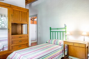 Un dormitorio con una cama, un aparador de madera, un cabecero verde y una mesita de noche con lámparas.