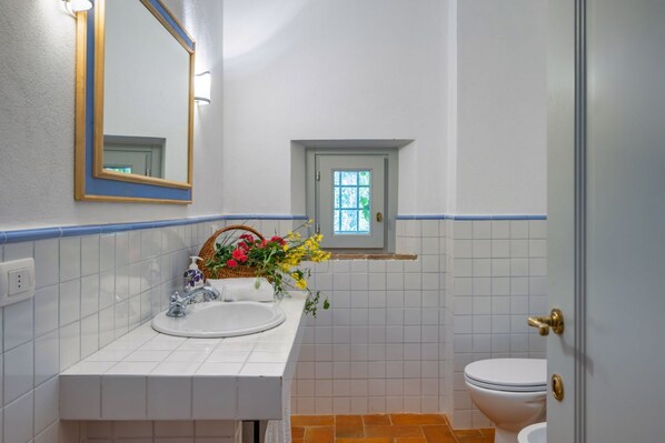 A bathroom with a white sink, a mirror, a small window, and a toilet.