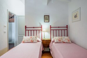 A bedroom with two beds, a nightstand, a lamp, and a framed picture on the wall. - Stunning villa of 200 sqm located on two levels, can accommodate up to 6 people. The property includes a private garden surrounded by olive trees, perfect for relaxing and organizing bike or horse rides in the quiet countryside of Castelnuovo Berardenga. (Castelnuovo Berardenga)