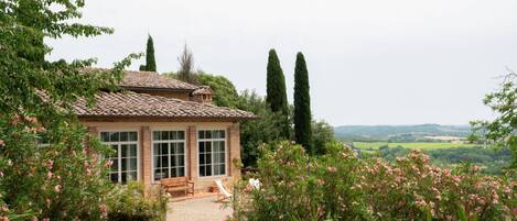 A house with a tiled roof, large windows, and a garden with pink flowers.