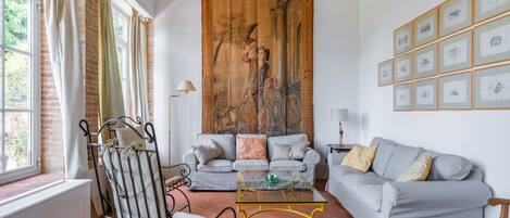 Una sala de estar con sofá, sillón y mesa de centro, un cuadro grande en la pared y fotografías enmarcadas.