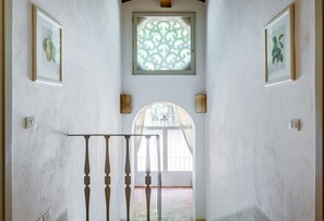 Un pasillo con una escalera, obras de arte enmarcadas, un ventanal decorativo y una puerta que da a un espacio exterior.