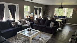 Una sala de estar con un sofá de color oscuro, una mesa de centro y un comedor con una mesa y sillas.
