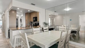 A modern kitchen with wooden cabinets, a central island, and a dining area with a white table and chairs.