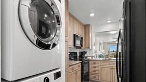 A compact kitchen with a washer and dryer, wooden cabinets, a microwave, and a refrigerator.