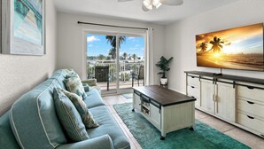 A living room with a sofa, a coffee table, a TV, and a balcony with a view of the ocean.