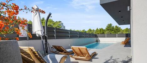 A rooftop pool area with wooden loungers and a covered seating area.