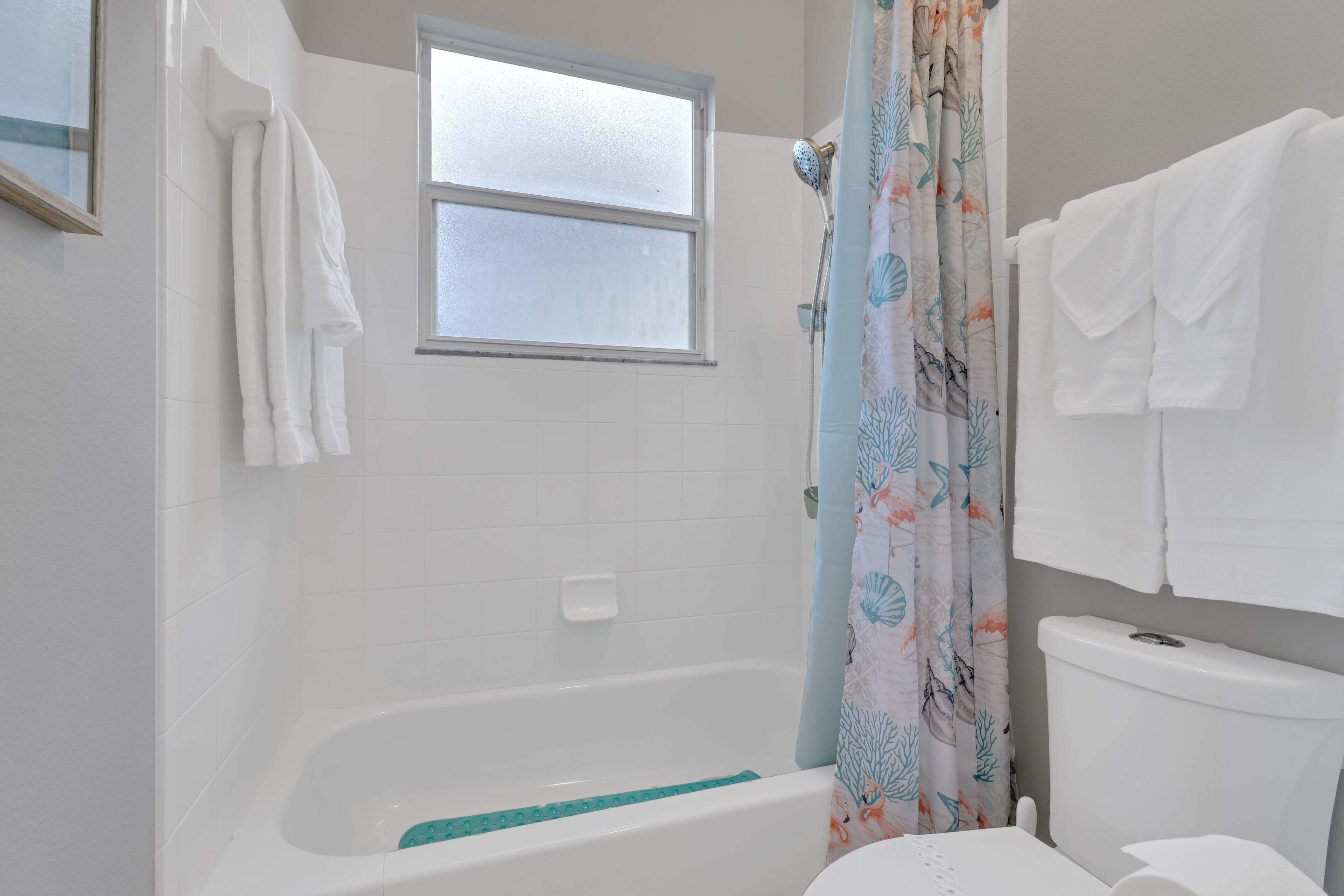 A bathroom with a bathtub, a window, a toilet, and a shower curtain.