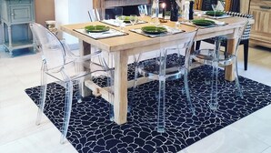 Un comedor con una mesa de madera dispuesta para cuatro personas, rodeada de sillas transparentes. Un cráneo de toro decora la pared sobre la chimenea.