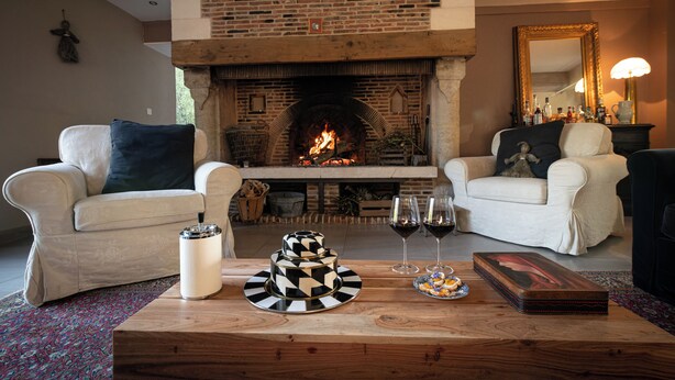 Una sala de estar acogedora con una chimenea de ladrillo, dos sillones blancos, una mesa de centro con adornos y un espejo.