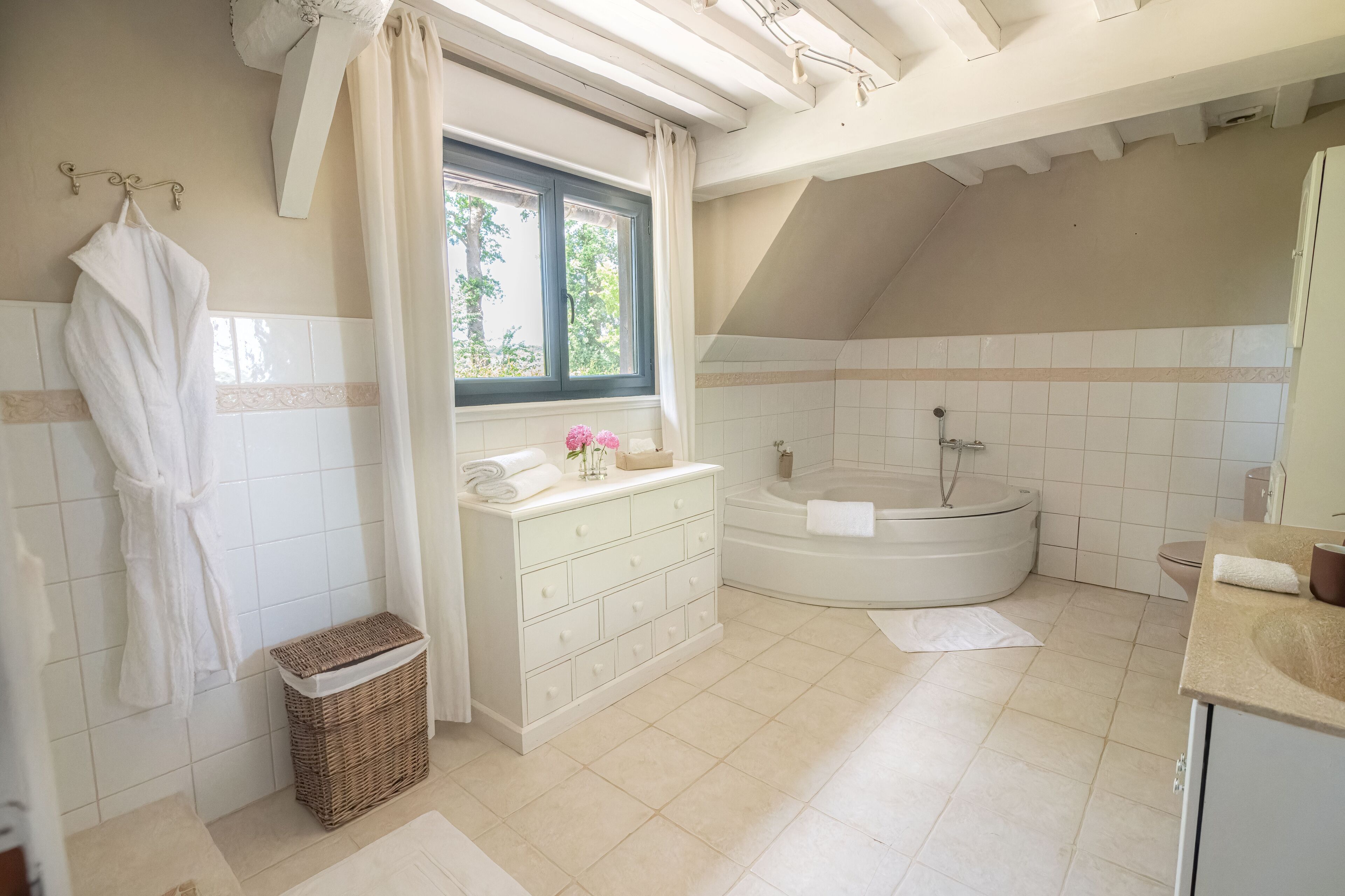 A modern bathroom with a freestanding bathtub, a vanity with a mirror, and a window with curtains.