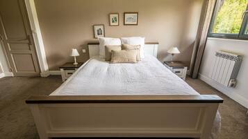 A bedroom with a large bed, two bedside tables with lamps, a radiator, and framed pictures on the wall.