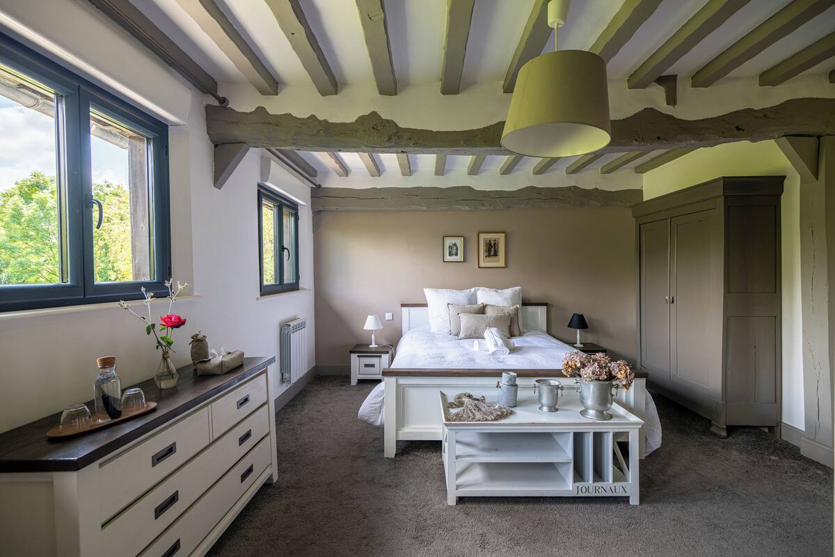 Un dormitorio con cama, mesitas de noche, cómoda, ventana y puerta.