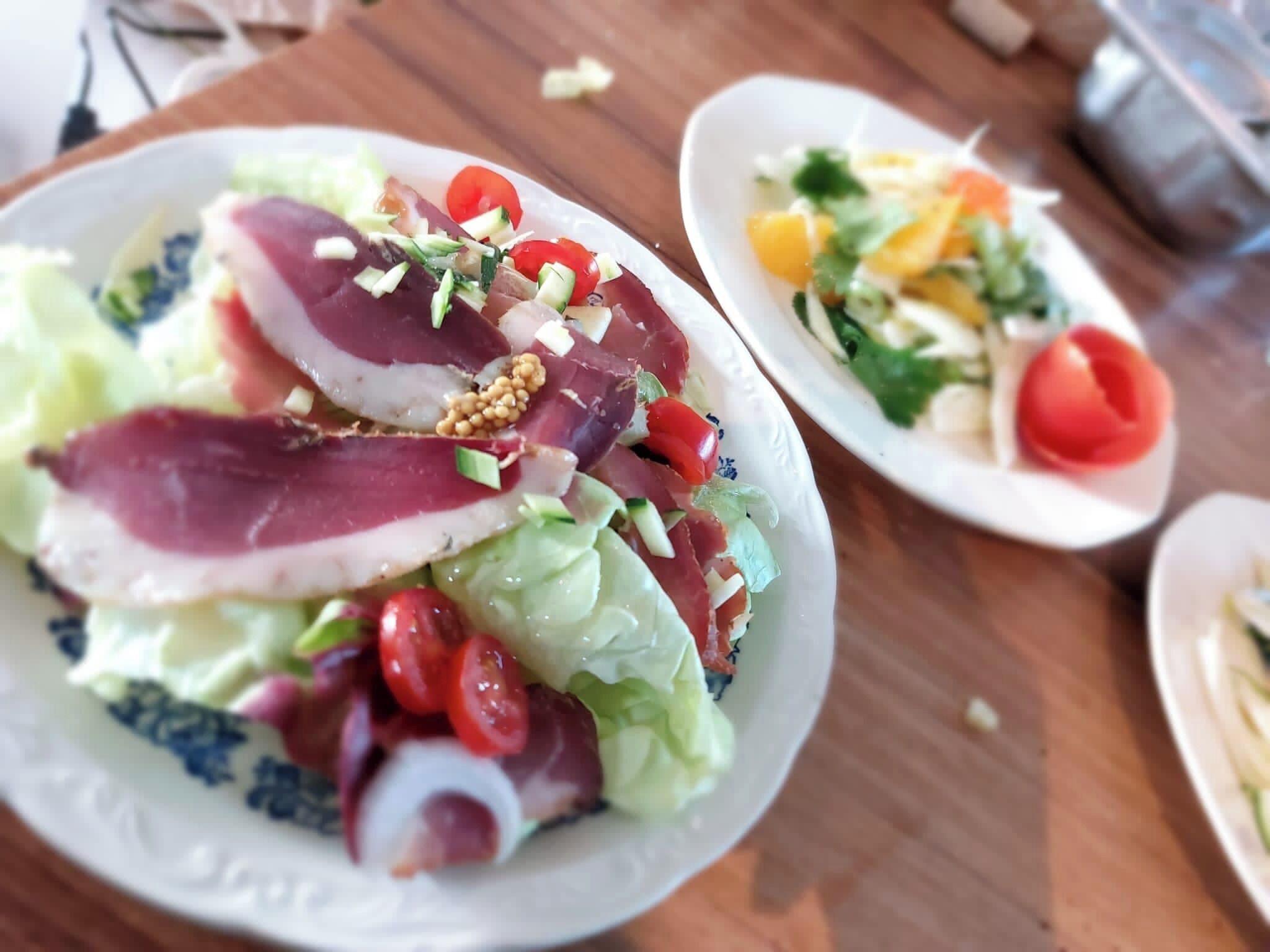 Ett bord med två tallrikar mat, den ena med en sallad och den andra med en rätt bestående av frukt och grönsaker.
