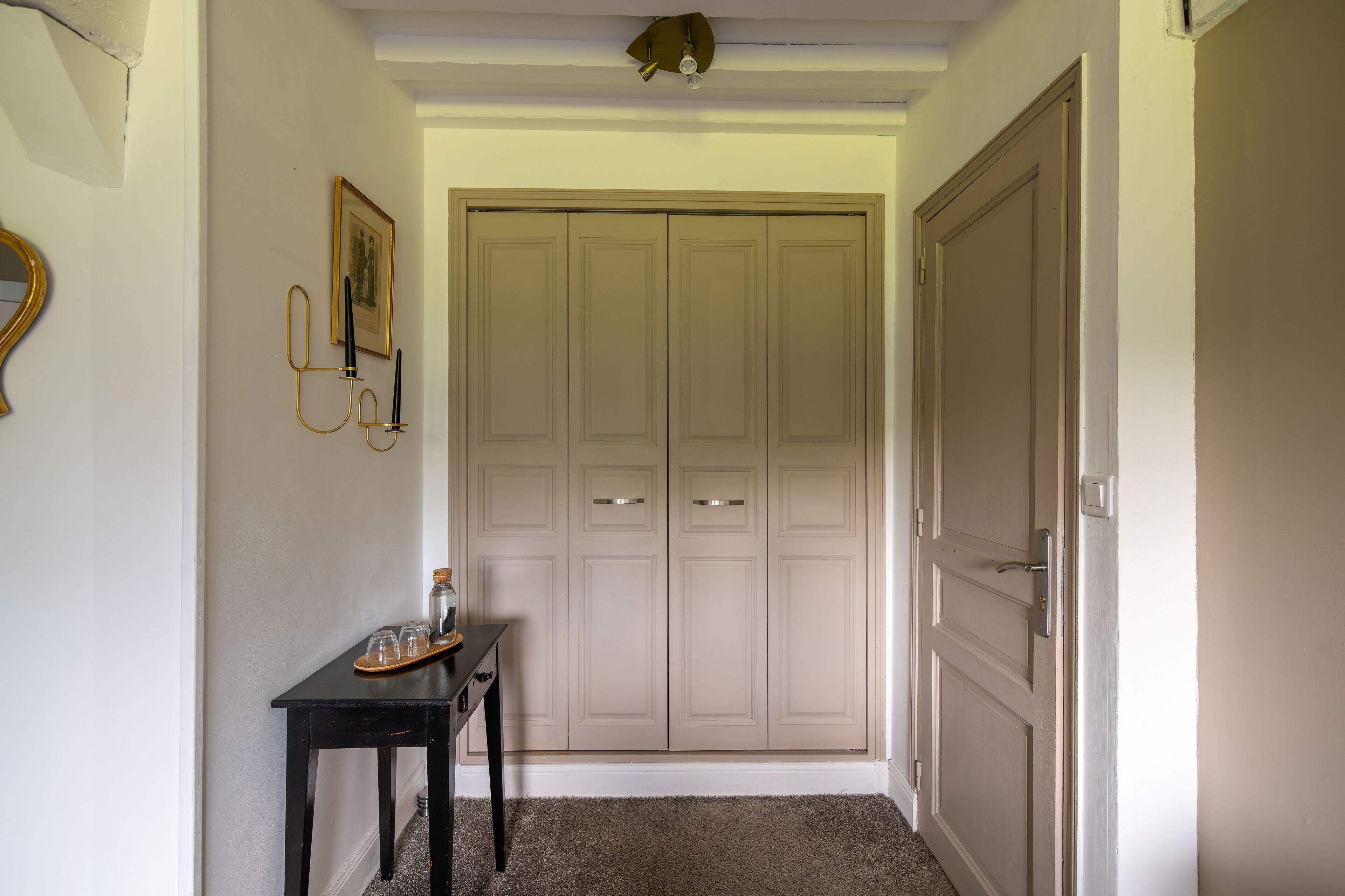 A hallway with a closed door, a small table with a tray, and a wall-mounted picture.